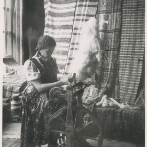 stoisko z tkaninami, pośrodku kołowrotek do przędzenia, przy nim kobieta w ludowym stroju