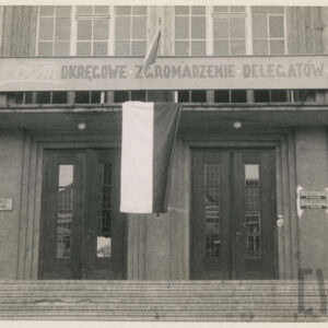 wejście do budynku, pomiędzy dwiema parami drzwi polska flaga, nad wejściem napis