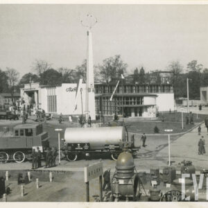 duży plac, na nim murowany budynek z przeszkleniami, przy budynku murowana kolumna o kwadratowej podstawie, zwężająca się ku górze, na ścianie napis „Społem”, na pierwszym planie urządzenia, lokomotywa i wagon cysterna, chodnikami spacerują ludzie
