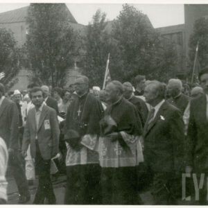 sześciu mężczyzn idących na czele maszerującego tłumu, dwóch z nich, idących w środku nosi szaty duchownych katolickich