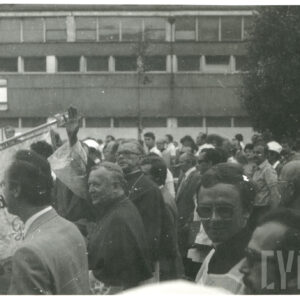 grupa ludzi, w tym osoby duchowne, w pochodzie ulicą wzdłuż hali fabrycznej