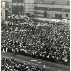 tłum ludzi zgromadzony na ulicy, pomiędzy budynkami mieszkalnymi przy tymczasowym ołtarzu polowym zbudowanym na rusztowaniu; ludzie uczestniczą w mszy świętej