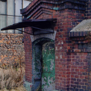 fragment elewacji z wejściem do ceglanego budynku, na drzwiach łuszcząca się farba