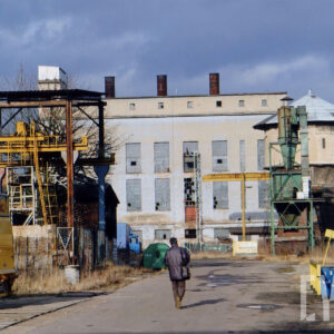 droga na terenie zakładów, w głębi murowany budynek z wysokimi oknami, z prawej wieża ciśnień