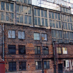 wysoka, długa przeszklona hala warsztatowa, przed nią dobudowany niższy, ceglany budynek