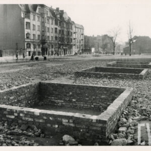 na pierwszym planie skwer z trzema pustymi piaskownicami, w głębi kilkukondygnacyjne kamienice