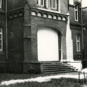 fragment dolnej partii elewacji ceglanego budynku z zamurowanym wejściem i bogatym detalem architektonicznym