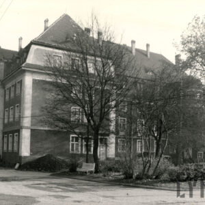 trzypiętrowy budynek, przed nim teren zielony z drzewami