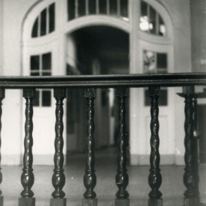 fragment wnętrza z drewnianą balustradą, w głębi duże łukowe drzwi szklano-drewniane