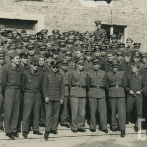 grupa mężczyzn w mundurach stoi przed nieotynkowanym budynkiem