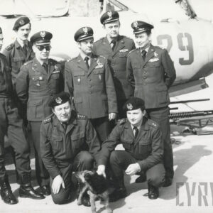 grupa mężczyzn w mundurach (dwóch z przodu kuca, przy nich siedzi pies) pozują do fotografii na tle samolotu