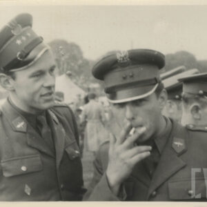 na pierwszym planie dwóch mężczyzn w mundurach wojskowych, mężczyzna z prawej pali papierosa