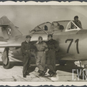 trzech mężczyzn w mundurach pozuje do zdjęcia przy samolocie wojskowym, czwarty mężczyzna widoczny za samolotem na wysokości kabiny