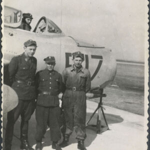 trzech mężczyzn w mundurach stoi przy samolocie, widoczny jego przedni fragment, w kabinie samolotu siedzi mężczyzna w mundurze