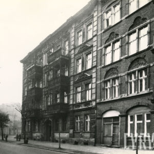 dwie, stykające się ze sobą kamienice, z lewej kamienica z bogato zdobionymi balkonami z elementami metalowymi