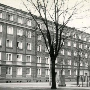 pięciokondygnacyjny budynek, na pierwszym planie drzewa pozbawione liści