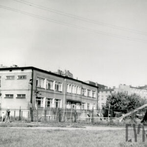 dwukondygnacyjny budynek otoczony terenem zielonym, z prawej plac zabaw dla dzieci ze zjeżdżalnią