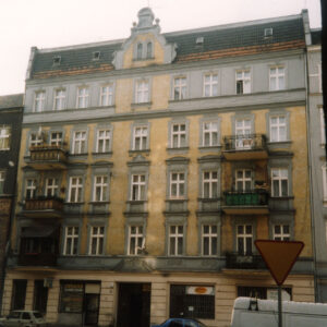 pięciokondygnacyjna kamienica, na chodniku wzdłuż ulicy zaparkowane samochody