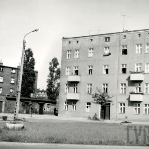 z prawej kilkukondygnacyjny budynek mieszkalny z balkonami, otynkowany, z lewej budynek nieotynkowany, ceglany