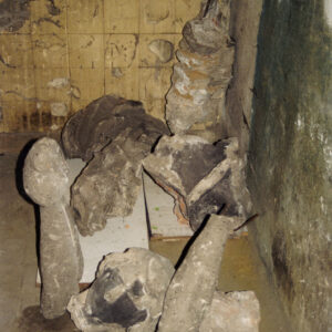 fragmenty zniszczonej kamiennej rzeźby leżące na posadzce i częściowo oparte o ścianę