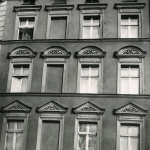 fragment elewacji kamienicy z oknami, nad oknami dekoracja rzeźbiarska
