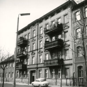 czterokondygnacyjna kamienica z balkonami, przed kamienicą, na chodniku zaparkowany samochód osobowy