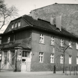 dwukondygnacyjny budynek ze spadzistym dachem, z lewej przybudówka i metalowa brama