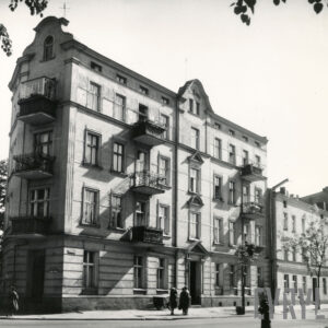 narożna, kilkukondygnacyjna kamienica z balkonami, ozdobnymi szczytami i dekoracją architektoniczną na elewacji