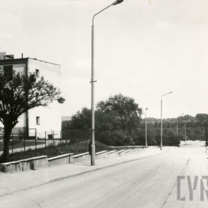 ulica schodząca w dół, z lewej fragment kilkukondygnacyjnego budynku, na chodniku latarnie uliczne