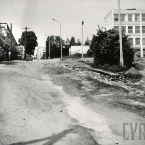 gruntowa droga idąca nieco pod górę, z prawej fragment czterokondygnacyjnego budynku