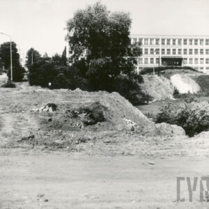 na pierwszym planie gruntowa, rozkopana droga, w głębi czterokondygnacyjny, prosty budynek