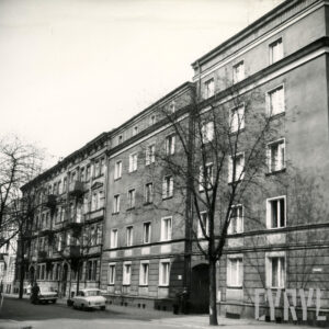 z prawej czteropiętrowy budynek mieszkalny, z lewej przylegająca do niego trzypiętrowa kamienica, przed nimi drzewa, na chodniku dwa zaparkowane samochody