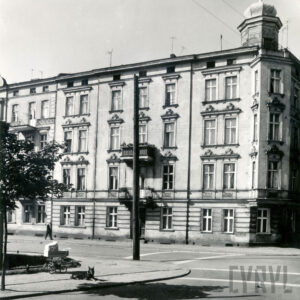 narożna, trzypiętrowa kamienica, wykusz na narożniku, narożnik przykryty hełmem, na chodniku wózek dziecięcy, przy nim leży pies