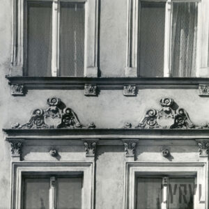 fragment elewacji kamienicy z oknami, nad nimi dekoracja rzeźbiarska
