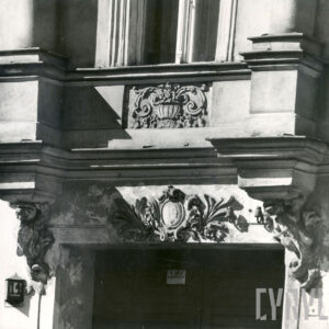 fragment elewacji kamienicy z dekoracją rzeźbiarską nad drzwiami i pod oknem