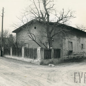 parterowy dom ze spadzistym dachem otoczony drewnianym płotem, na pierwszym planie nieutwardzona ulica