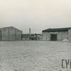 dwie murowane stodoły ze spadzistymi dachami, na pierwszym planie pola