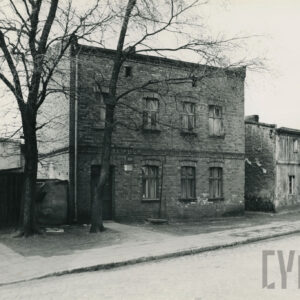 piętrowy, ceglany dom ustawiony wzdłuż wybrukowanej ulicy, po prawej drugi, mniejszy, parterowy dom z poddaszem