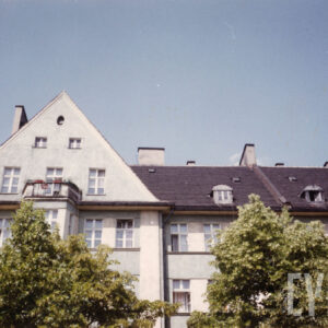 ostatnie piętra domu, z lewej trójkątny szczyt, pod nim wykusz zakończony balkonem, fragmenty górnej partii drzew