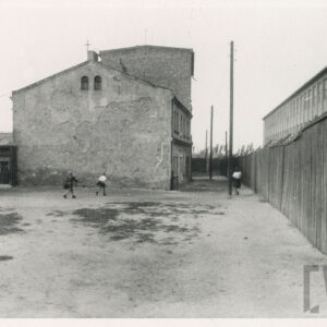 dwukondygnacyjne, ceglane budynki, z prawej drewniane ogrodzenie, za nim fragment fabrycznej hali