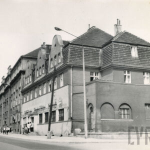 trzykondygnacyjny, narożny budynek mieszkalny z mansardowym dachem, na poziomie pierwszego piętra uskok w elewacji z balkonem