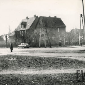 kilkupiętrowa willa, otoczona ogrodem i ogrodzona metalową siatką, na pierwszym planie skrzyżowanie ulic