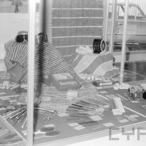 za witryną widoczne różne przedmioty: druty do włóczki, koc, szczotki i grzebienie