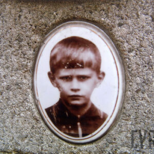 Medalion portretowy ze zdjęciem w kolorze sepii. Chłopiec w koszuli z kołnierzykiem. Włosy jasne, proste z grzywką.