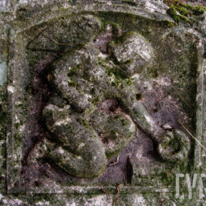 Płaskorzeźba nagiego uskrzydlonego anioła, który przyklęka i składa wieniec na trumnie. Omszona i zabrudzona. Po bokach wyryte kwiaty.