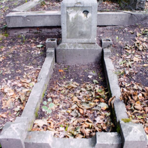 Mogiła obmurowana. Na cokole stoi postument bez zwieńczenia. Po jego bokach słupki z otworami na kwiaty. Z tyłu inny nagrobek, fragmenty krzyży i pni drzew.