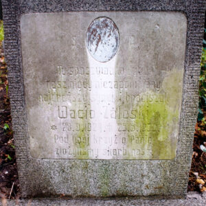 Zabrudzona biała tablica z napisami i śladem po medalionie portretowym wtopiona w płytę nagrobną. 