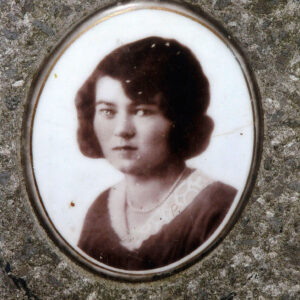 Dobrze zachowany medalion ceramiczny z portretem. Kobieta o krótkich ciemnych włosach, w ubraniu z białym wykończeniem przy szyi i naszyjnikiem.