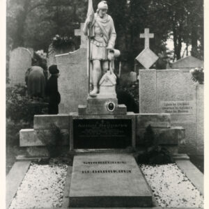 Duży nagrobek obmurowany z kamienną płytą po środku. Po bokach wysypane białe kamyczki. Płyta nagrobna z czarną tablicą z napisami. Na niej figura św. Floriana. Z tyłu inne nagrobki i drzewa.   