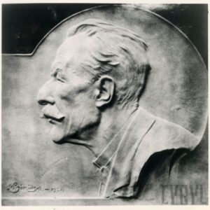 Płaskorzeźba z wizerunkiem mężczyzny. Włosy zaczesane do tyłu, wąsy, ubrany w marynarkę.